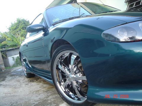 1995 Mazda MX-6 - Teal 1995 Mazda MX-6 coupe, front passenger side, with chrome wheels and aftermarket body kit.