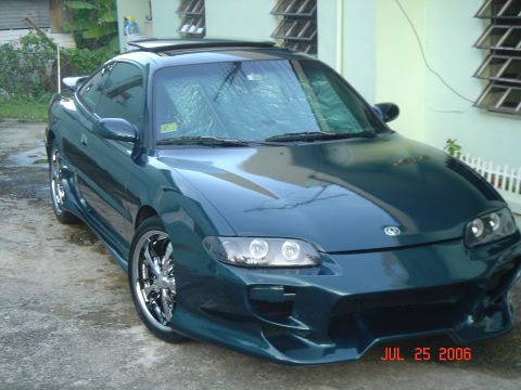 1995 Mazda MX-6 - A dark teal coupe with an aggressive aftermarket body kit and chrome wheels is parked on a concrete driveway.