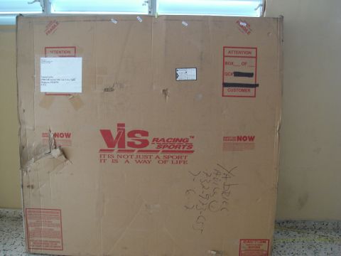 1995 Mazda MX-6 - A large cardboard box, likely containing automotive parts, is shown with various shipping labels and branding visible.