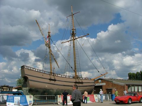 2001 Ford Fiesta - A large sailing vessel is displayed outdoors, with a red convertible parked nearby and people observing the scene.