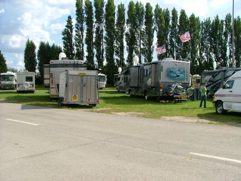 2001 Ford Fiesta - A collection of recreational vehicles are parked in a grassy area, with a line of tall trees behind them.