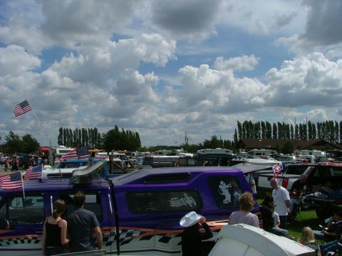 2001 Ford Fiesta - A crowd gathers around a custom purple van adorned with American flags at an outdoor event.