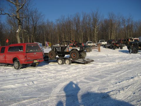 1991 Ford Bronco - Several vehicles are parked in a snowy lot, with one custom off-road buggy loaded onto a trailer.