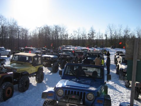 1991 Ford Bronco - A large group of off-road vehicles are parked in the snow on a clear day.