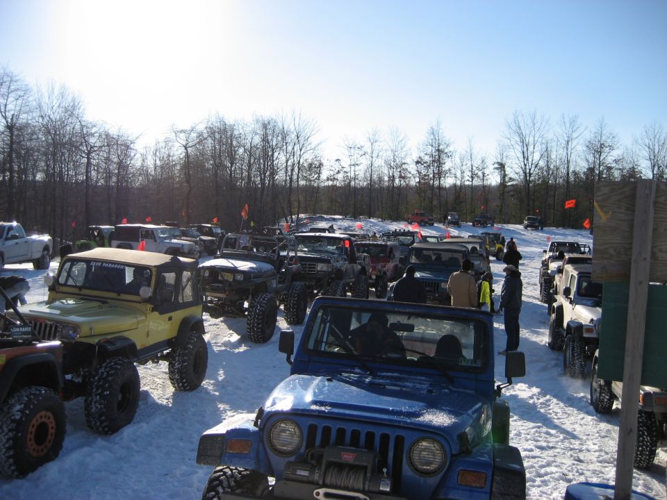 Many off-road vehicles parked in a snowy field with trees in the background