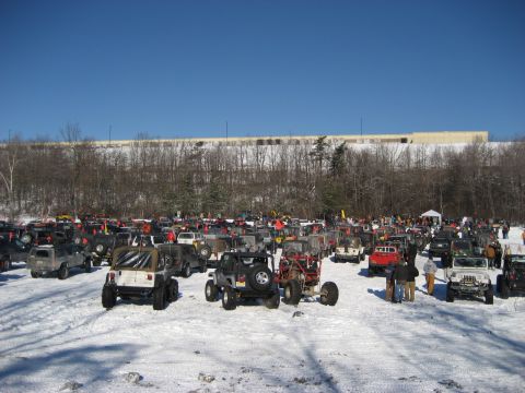 1991 Ford Bronco - A large gathering of off-road vehicles are parked in a snow-covered lot under a clear blue sky.