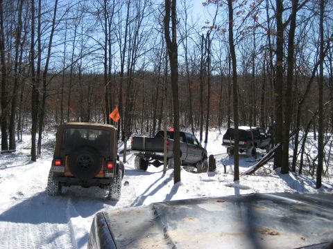 1991 Ford Bronco - Multiple off-road vehicles navigate a snowy trail through a forest.