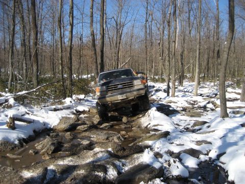 1991 Ford Bronco - This 1991 Ford Bronco is tackling a challenging off-road course in a wooded area with snow on the ground.