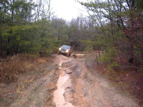 1991 Ford Bronco - Ford Bronco tackles a challenging muddy off-road path through a dense forest.