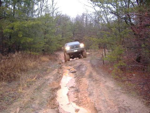 1991 Ford Bronco - A gray Ford truck navigates a challenging muddy path in a wooded area.