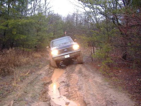 1991 Ford Bronco - A 1991 Ford Bronco navigates a muddy path through a wooded area.