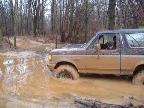 1991 Ford Bronco - This 1991 Ford Bronco is navigating a challenging muddy path in a wooded area.