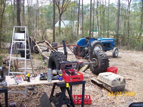 1978 Ford Bronco - A tractor chassis is being worked on outdoors, with tools laid out and a blue tractor visible in the wooded area.