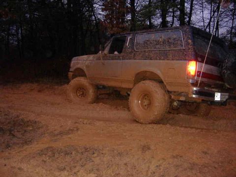 1991 Ford Bronco - This SUV is covered in mud while driving on a dirt path through the woods.