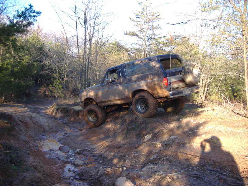 Mud-covered dark SUV driving off-road on a dirt track with trees in the background
