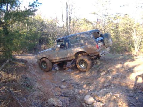 1991 Ford Bronco - A muddy Ford Bronco navigates a challenging off-road trail.