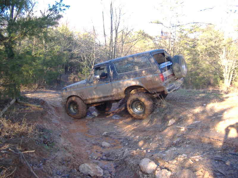 Mud-covered Ford Bronco on a dirt trail, with a spare tire mounted on the rear