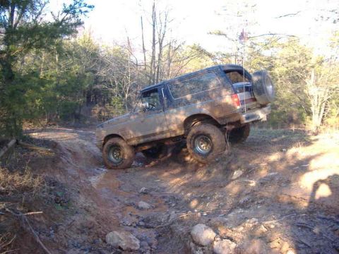 1991 Ford Bronco - This 1991 Ford Bronco navigates a challenging off-road course, its tires kicking up mud on the steep incline.