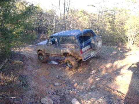 1991 Ford Bronco - A 1991 Ford Bronco navigates a muddy off-road trail, kicking up dirt as it goes.