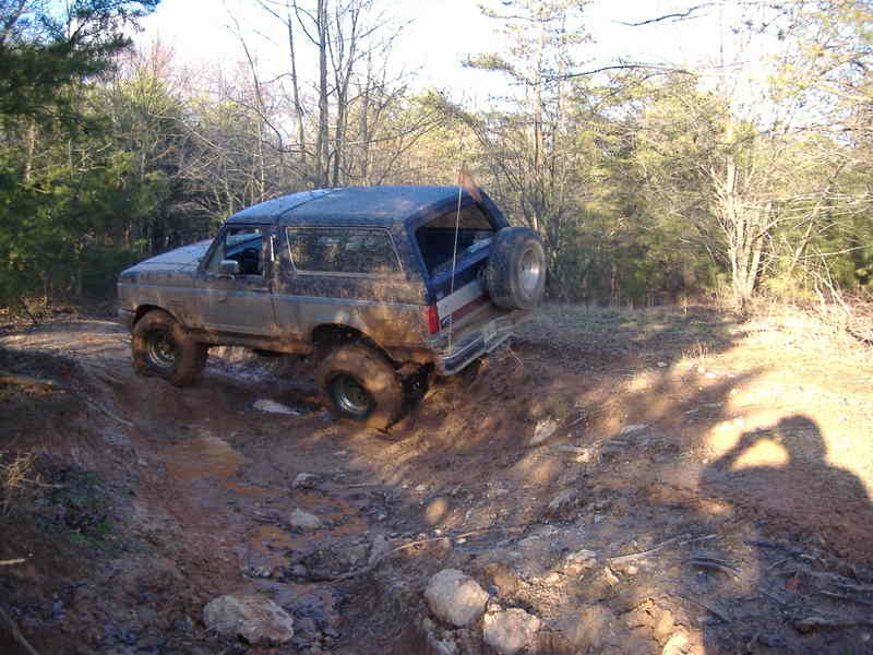 Mud-covered Ford Bronco driving off-road, spare tire mounted on rear door