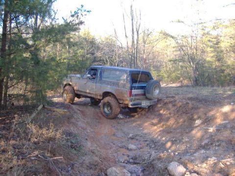 1991 Ford Bronco - This Ford Bronco, likely from the late 1980s, tackles a challenging muddy terrain with its off-road tires.