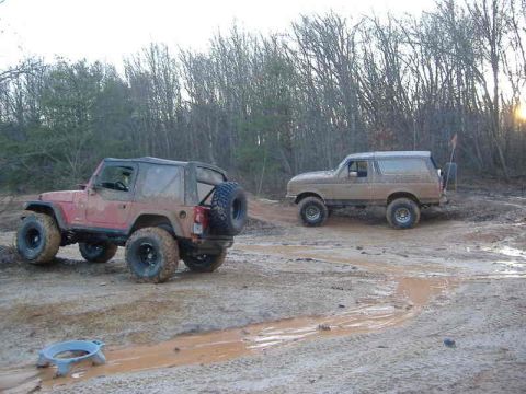 1991 Ford Bronco - Two off-road vehicles navigate a muddy terrain under a cloudy sky.