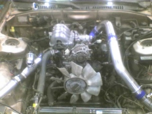 1991 Mazda RX-7 - A close-up view of a modified engine bay, showing custom turbo piping and cooling components.