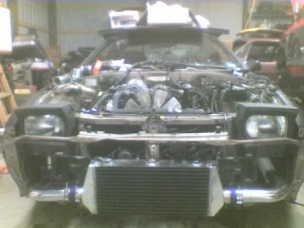 1991 Mazda RX-7 - Front view of a Mazda RX-7 undergoing modifications, an aftermarket intercooler and exposed engine components.