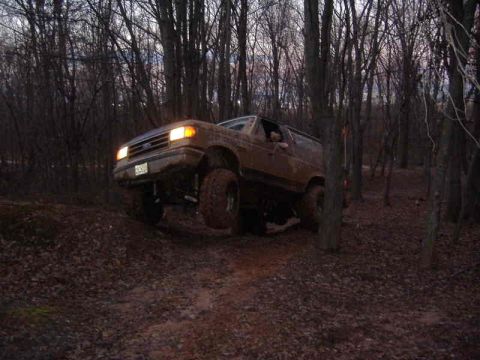 1991 Ford Bronco - 1991 Ford Bronco navigating a wooded trail with its front wheels off the ground.