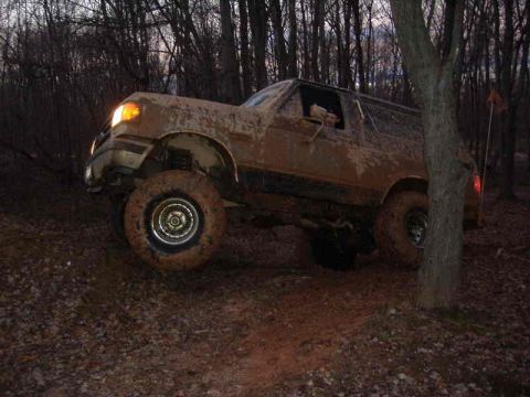 1991 Ford Bronco - 1991 Ford Bronco navigating a muddy off-road trail in a wooded area.
