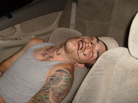 1992 Ford Bronco - A man is passed out in the back seat of a car, with writing on his face and a large tattoo on his arm.
