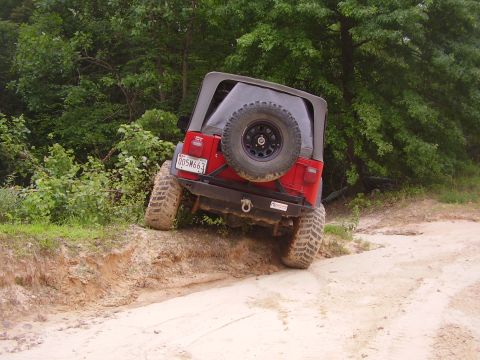 1991 Ford Bronco - A red Jeep Wrangler navigates an off-road trail, its rear tire angled precariously.