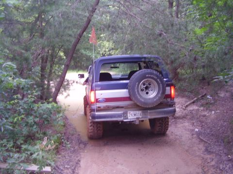 1991 Ford Bronco - Ford Bronco navigating a wooded dirt path, showing its rear end and spare tire.