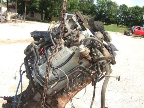 1900 Ford 427 - Engine assembly, likely from a truck, is hoisted by chains in an outdoor yard.