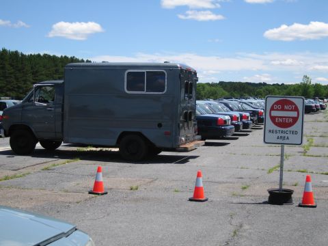 1991 Ford LTD Crown Victoria - A gray utility van is parked in a lot alongside a line of blue sedans, with a restricted area sign visible.