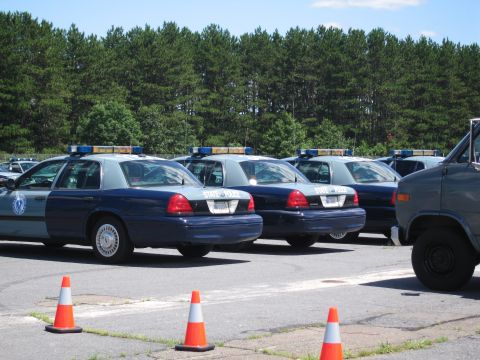 1991 Ford LTD Crown Victoria - A line of police cruisers are parked in a lot, with a van visible on the right side of the frame.