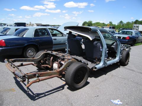 1991 Ford LTD Crown Victoria - The stripped chassis of a car sits in a lot, with other vehicles visible in the background.
