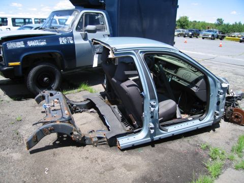 1991 Ford LTD Crown Victoria - The stripped body of a car sits in a junkyard, revealing its interior and chassis.