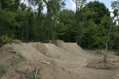 1997 Ford Probe - Dirt jumps are set up in a wooded area, with a Supermotors.net logo visible in the lower right corner.