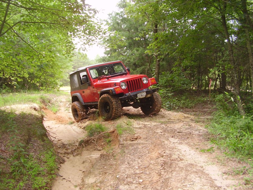 Red Jeep Wrangler navigating a muddy off-road trail
