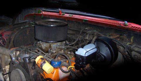 1978 Ford Bronco - The engine bay of a red vehicle shows a large air filter and carburetor, with brake components visible.