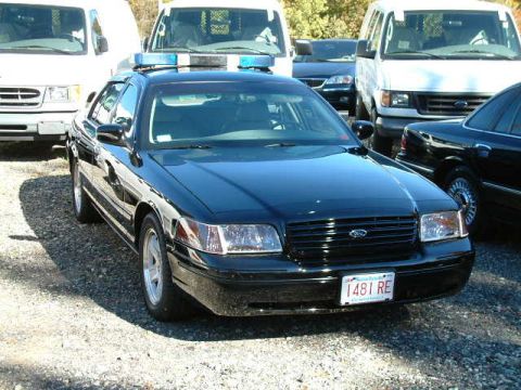 2002 Ford Crown Victoria - A black 2002 Ford Crown Victoria police car is parked outdoors, a light bar on the roof and a visible license plate.