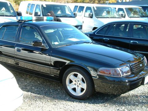2002 Ford Crown Victoria - Black 2002 Ford Crown Victoria police car with blue light bar, parked outdoors.