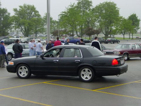 2002 Ford Crown Victoria - A black 2002 Ford Crown Victoria sedan is parked in a lot with other vehicles and people.