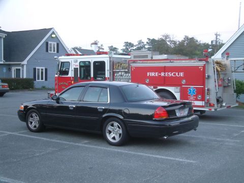 2002 Ford Crown Victoria - A black 2002 Ford Crown Victoria LX Sport is parked in a lot next to a fire truck.