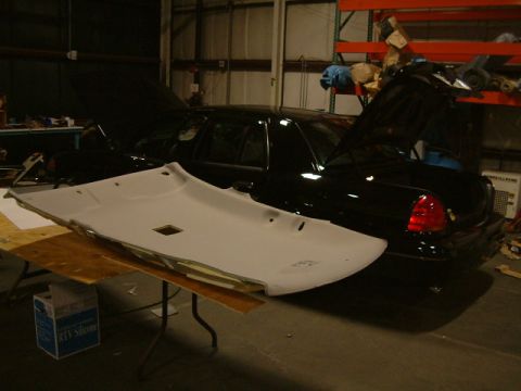 2002 Ford Crown Victoria - A black 2002 Ford Crown Victoria is shown with its hood and trunk open, while a removed headliner rests on a table in front of it.