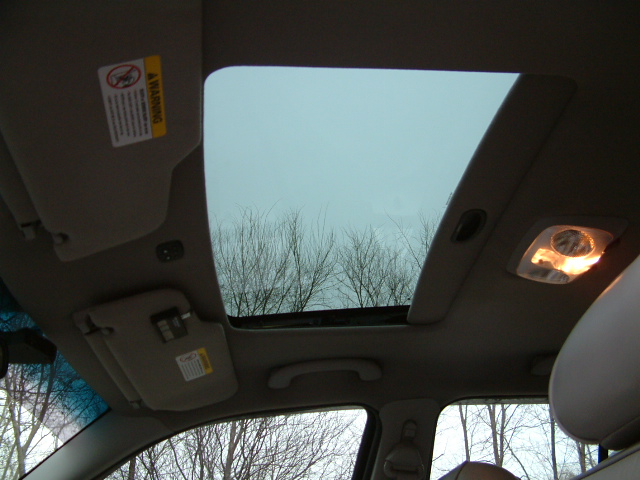 Open sunroof viewed from inside a car with tan headliner and dome light lit