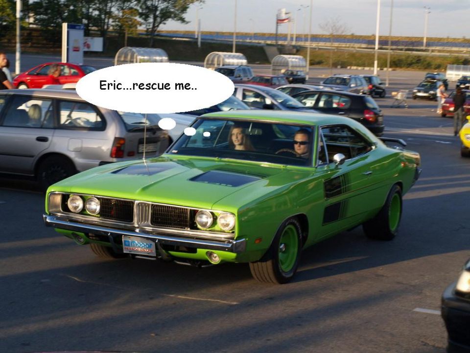 Lime green 1969 Dodge Charger with black stripes, two people inside, driving in a parking lot