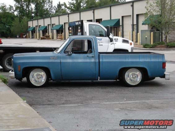 Blue lowered Chevrolet square-body short-bed pickup with polished wheels, side view in a parking lot