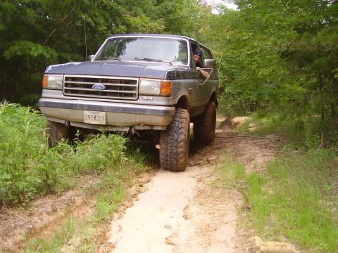1991 Ford Bronco - A Ford Bronco navigates a muddy trail, its off-road capabilities with large tires and lifted suspension.